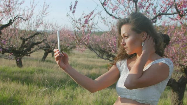 Attractive girl doing selfie on the background of flowering trees