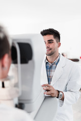 Naklejka na ściany i meble Male optometrist checking patient's vision at eye clinic. Medical examination.