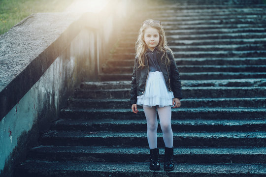 Stylish little girl in black leather jacket and white skirt posing outdoor