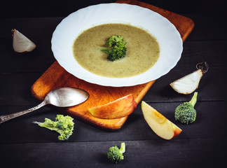 Soup puree with broccoli and apple in a white plate on a dark background with  onion and spoon