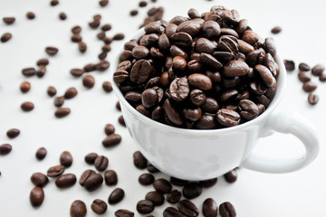 Coffee beans in white cup and some fall down spread on white background. Sellected focus.