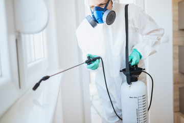 Exterminator in work wear spraying pesticide with sprayer.
