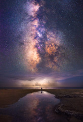 Milky way and storm reflected in the water with small person bellow
