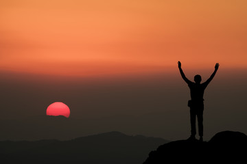 Silhouette of man hold up hands on the peak of mountain