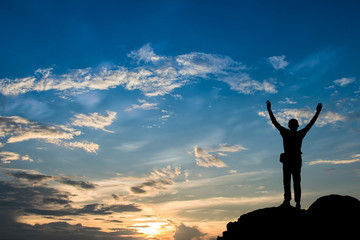 Silhouette of man hold up hands on the peak of mountain.