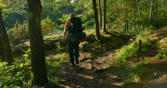 Sporty man with large backpack walks down steep mountain path at sunset