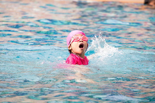 Smiling baby girl wearing swimming glasses in swimming pool.