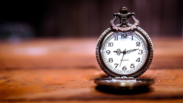 old antique pocket watch showing time on wooden floor with blurred background