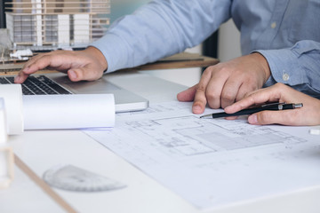 Engineering or Creative architect in construction project, Engineers hands working on construction blueprint and building model at a workplace in office, Building and architecture concept