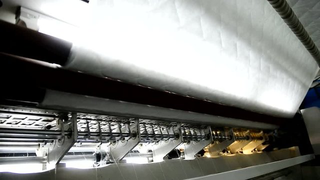 Stitching fabric for orthopedic mattress in factory indoors. producing slipcover from white textiles in premises of modern plant produces mattresses