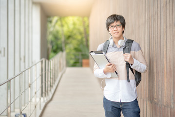 Young Asian man dressed in casual style holding file and laptop computer in university, smiling male student in college