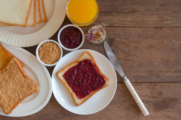 Toast bread with homemade strawberry jam and peanut butter served with orange juice. Homemade toast bread with jam and peanut butter on table for breakfast. Delicious toast bread in top view flat lay.