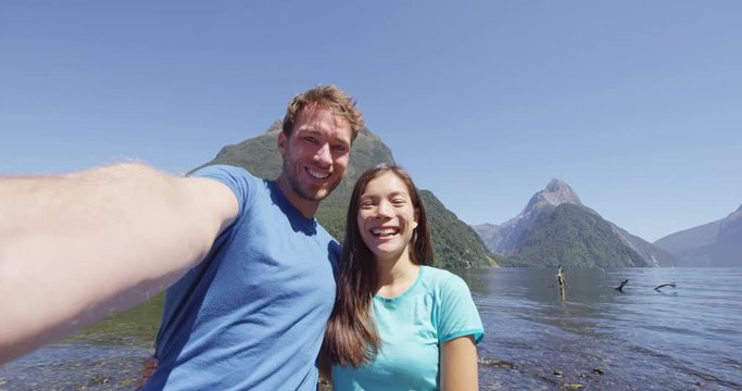 Couple taking selfie video having fun on travel in New Zealand, Milford Sound. Happy woman and man in love travelling taking candid self portrait video, Fiordland, New Zealand. SLOW MOTION.