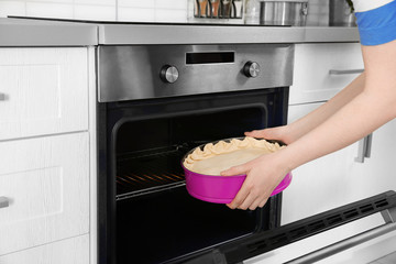 Young woman putting baking dish with pie into oven. Concept of cooking classes