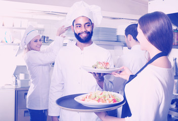 Waitress and crew of professional cooks posing at restaurant