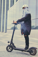 A man vaping and riding by electric scooter.