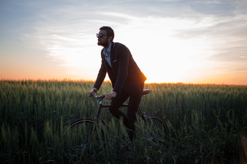 A caucasian businessman riding a bicycle in summer fields, Male in business suit ride on fixie bike.