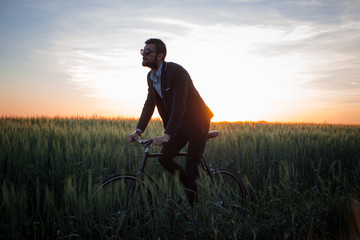 Fototapeta premium A caucasian businessman riding a bicycle in summer fields, Male in business suit ride on fixie bike.