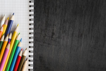 White notebook with color pencils on the dark table. Art concept. Top view. Empty place for a text or drawing on the black background.