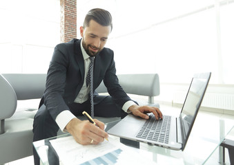 Stylish man working on laptop and making notes in notebook