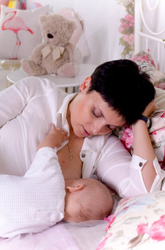 Breastfeeding baby. Young mother holding her newborn child. Mom nursing baby. Woman and new born boy in white bedroom.