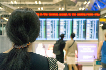 Asian woman backpackers in international airport terminal, looking at flight information board, checking her flight, holiday vacation travel concepts.