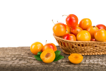 yellow plums with leaf in a wicker basket on wooden table with white background