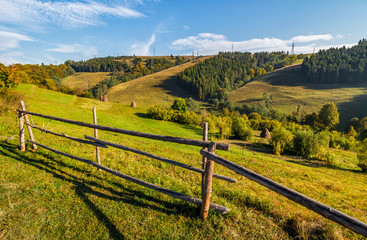 Fototapeta na wymiar hay stacks behind the fence on rural field. lovely Carpathian hilly countryside landscape near forest in early autumn morning