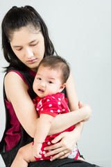 Mother holding her crying adorable baby on colorful eva foam indoors
