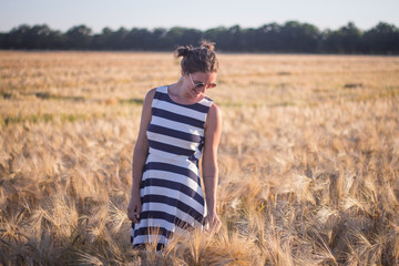 Young woman in dress and sunglass hawing good time in summer wheat fields