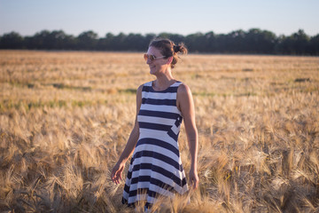 Naklejka na ściany i meble Young woman in dress and sunglass hawing good time in summer wheat fields
