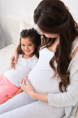 Pregnant woman hugging daughter on couch