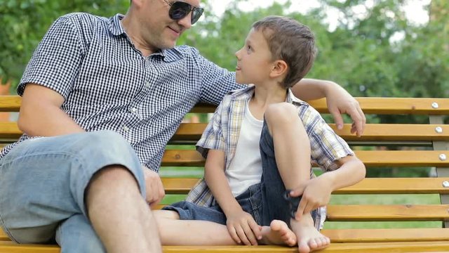 Father and son sitting on the bench in the park at the day time. They playing with spinner. Concept of friendly family.