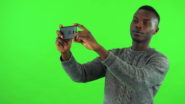 A young black man takes pictures of something off the camera with a smartphone - green screen studio