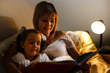 mother and child girl reading a book in bed before going to sleep