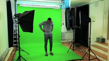 A young black man adjusts his clothes in a green screen studio