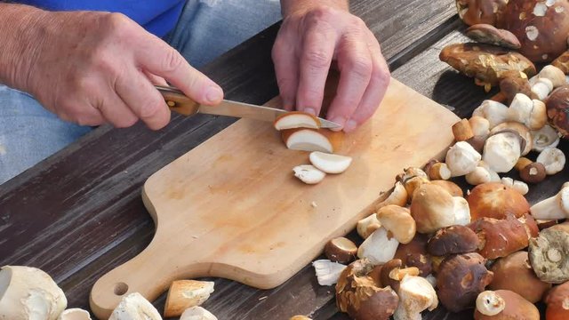 Nice wild mushrooms are cut with knife into small pieces on wooden chopping board. Man hands cut boletus slice on wooden table