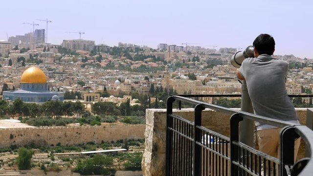 Tourist looks in binoculars tower viewer at the Jerusalem Old City view. Mount of Olives is a famous Holy Land place and it has a fantastic view to the Old Jerusalem