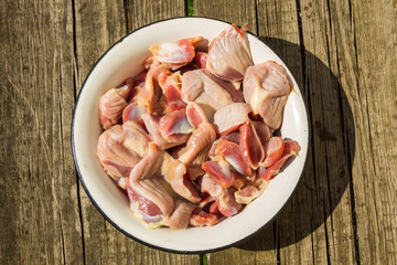 Raw chicken gizzards in metal enamelled bowl on rustic wooden table