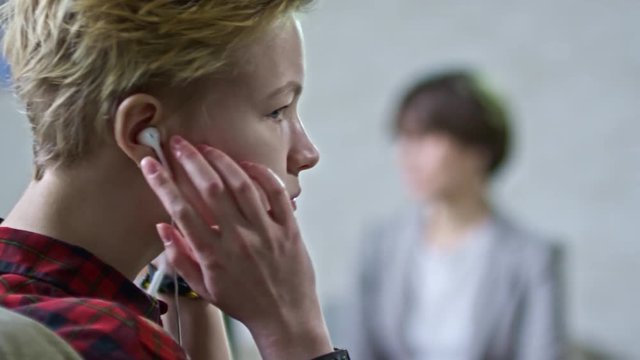PAN with rack focus of blond teenage girl with short hair putting on earphones and looking away as her frustrated mother gesturing and talking to female psychiatrist in glasses