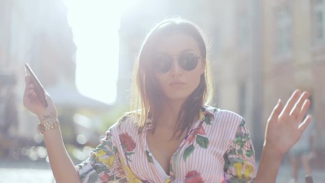 Summer portrait of young fashionable styled model gorgeus attractive girl in boho style clothes using phone and dancing on the old city architecture street, sun shining