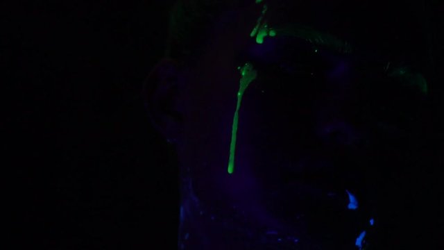 The girl smeared with paint on her face drips with a luminescent paint that glows in the ultraviolet light