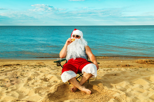 Santa Claus on the beach eating a hamburger.