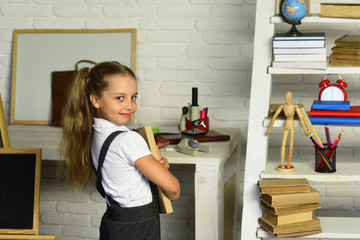 Schoolgirl holds textbook on light brick wall classroom background