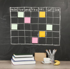 Grid timetable schedule with note paper on black chalkboard background.