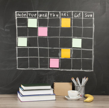Grid timetable schedule with note paper on black chalkboard background.