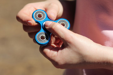 girl playing blue metal spinner in hands on the street, female hands holding popular fidget spinner toy on gray background, anxiety relief toy, anti stress and relaxation fidgets.