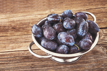 Fresh blue plums in rustic colander on old wooden table. Organic food. Copy space, toned