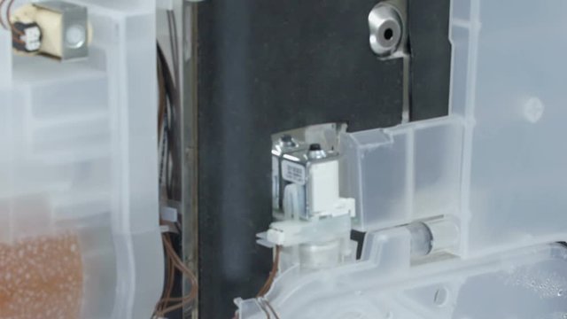 A repairman is pointing at a machine that he is about to repair. Something is wrong with a washing machine and a dryer.