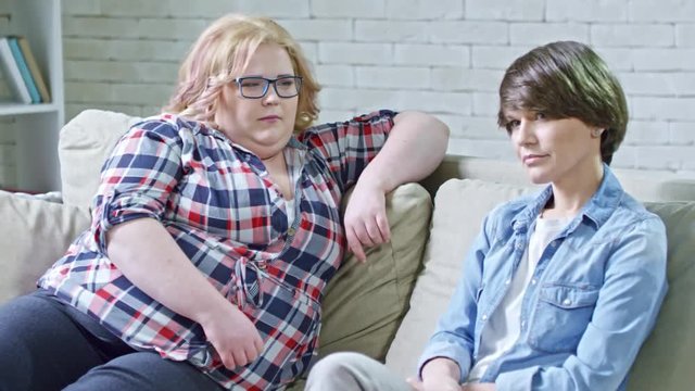 Zoom in shot of confident young woman and her obese female friend sitting on couch and listening to gesturing male psychotherapist explaining something